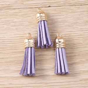 Three pieces of purple faux suede tassel pendants with golden metal caps on a wooden background