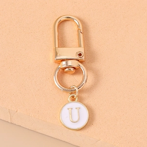 Detail of a gold metal keychain with white enamel round pendant featuring the letter U