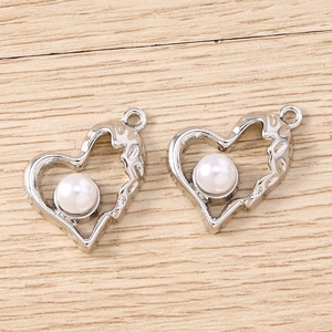 Dettaglio di ciondoli a cuore in metallo martellato argento con perla bianca e anello