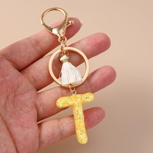 Detailed view of yellow resin letter T keychain with sparkles, gold clasp and white tassel