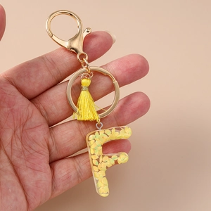Detail of letter F resin keychain with golden yellow sequins and matching silk tassel