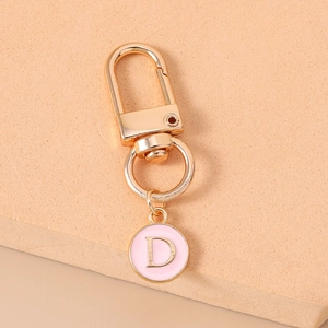 Detail of gold keychain with a round pink enamel pendant featuring the letter D