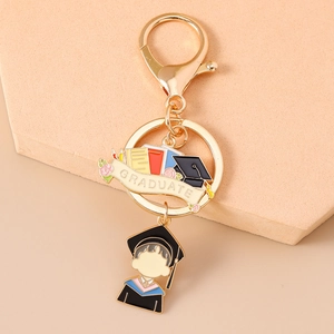Detail of a golden enamel graduation keychain with Graduate banner and student charm