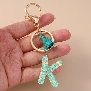Close-up of resin letter K keychain with green tassel and gold alloy hardware