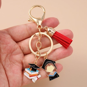Detail of graduation girl keychain with red tassel and golden doctoral cap held in hand
