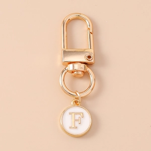 Detail of a golden lobster clasp and a round white charm with an engraved letter F