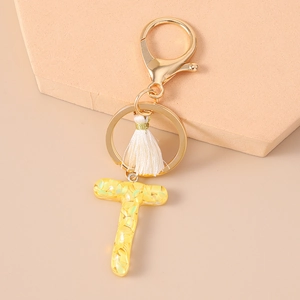 Detail of resin letter T keychain with gold sequins and white tassel on display