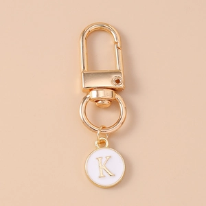 Detail of golden metal keychain featuring white enamel charm with letter K and lobster clasp