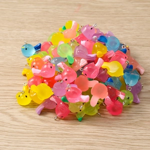 Macro view of colorful translucent resin bird charms with metal loops on wood background