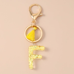 Detailed close-up of letter F resin keychain with yellow tassels and golden lobster clasp