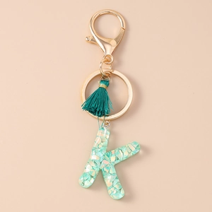 Detail of teal resin letter K keychain with iridescent sequins and green tassel