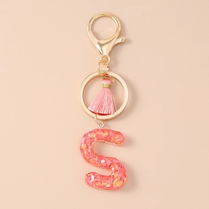 Detail of pink tassel keychain with resin letter S featuring sparkling sequins and gold clasp
