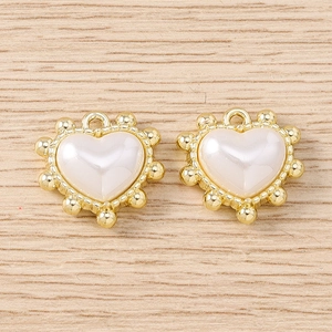 Dettaglio di pendenti a cuore in metallo dorato con perla sintetica e bordi a rilievo