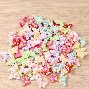 Macro detail of colorful resin butterfly charms with metal loops on wood background