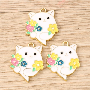Detailed view of three enamel flower cat charms on a light wood background for DIY jewelry