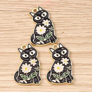 Detailed close-up of three black cat enamel charms with white daisy patterns on wood