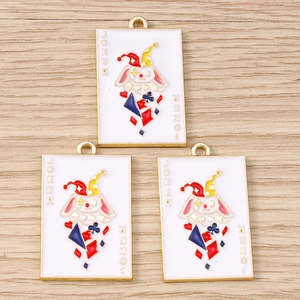 Gros plan de trois breloques Joker émaillées pour bijoux DIY sur fond de bois clair