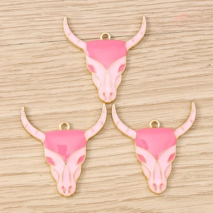 Dettaglio di ciondoli a teschio di toro in smalto rosa e oro per creazione di gioielli