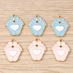 Detalle de dijes de huella con corazón en esmalte rosa y azul para joyería artesanal