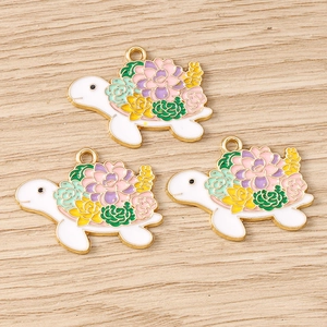 Macro view of three sea turtle pendants with colorful floral enamel on light wood background