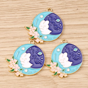 Macro shot of three rabbit and moon enamel charms on light wood texture background