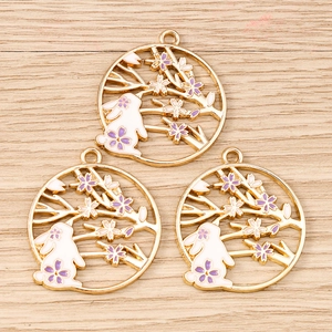 Detail of three gold rabbit pendants with white enamel and sakura flowers on wood surface
