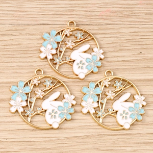 Macro view of three gold-plated rabbit and cherry blossom enamel pendants on wood