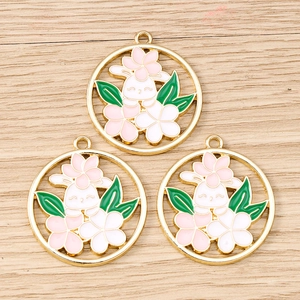 Macro detail of three enamel bunny and flower charms on a light wood background