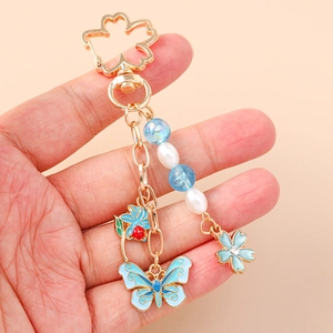 Golden flower and butterfly keychain with blue enamel charms and white faux pearls