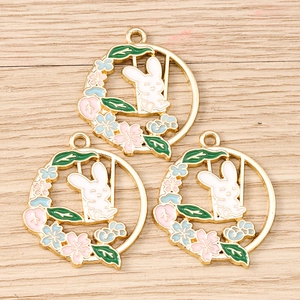 Macro detail of three enamel bunny wreath pendants on a light wood background