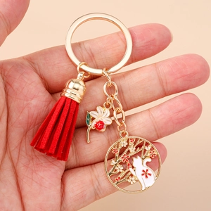 Close-up of golden cat and cherry blossom keychain with red tassel and petal charm