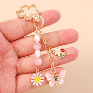 Golden floral keychain with pink daisy, butterfly charm and faux pearls held in hand