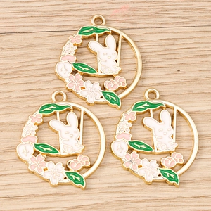 Three enamel bunny pendants with cherry blossoms and swings on a wooden surface