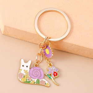 Detail of a snail enamel keychain with purple shell and floral patterns on a gold ring