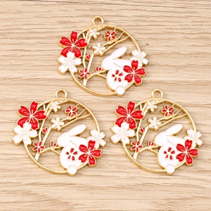 Detailed macro view of three golden bunny and cherry blossom enamel charms for DIY jewelry