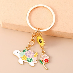 Detailed view of floral turtle keychain with sunflower and ladybug charms on a gold ring