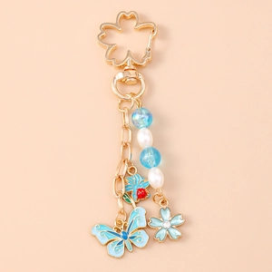 Close-up of gold butterfly and cherry blossom keychain with blue enamel and pearls