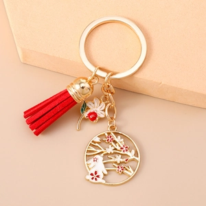 Close-up of golden Chinese style keychain with rabbit charm, plum blossoms, and red tassel