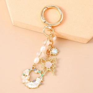 Exquisite pearl keychain with golden butterfly, star, and cat wreath charms on neutral background