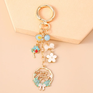 Detail of golden floral keychain with enamel daisy, bow, and Happy Holidays wreath charm