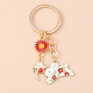 Detail view of gold keychain set featuring enamel red sunflower and white floral bunny charms