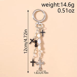 Detail of silver cross keychain with faux pearls and rhinestones on a beige background