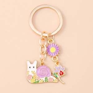 Detail of golden metal keychain featuring a colorful snail and purple flower pendant charms
