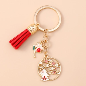 Exquisite gold rabbit keychain with red tassel and enamel flower charms on beige background