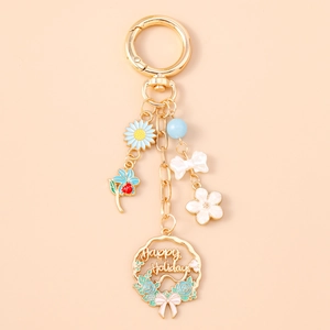 Detailed close-up of gold enamel keychain with floral charms and Happy Holidays wreath