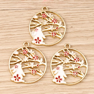 Three enamel rabbit and cherry blossom charms on a light wood background for DIY jewelry