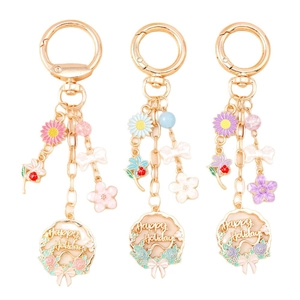 Golden enamel keychain set with colorful flowers bow and Happy Holidays charm on white background