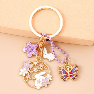 Dettaglio portachiavi dorato con fiore viola, coniglio bianco e farfalla di strass lucidi