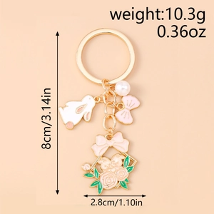 Détail d'un porte-clés doré avec breloque lapin blanc, nœuds roses et couronne de rose