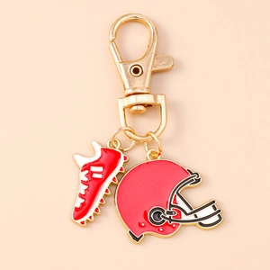 Detail of rugby helmet and shoe keychain pendants with red and white enamel on gold metal